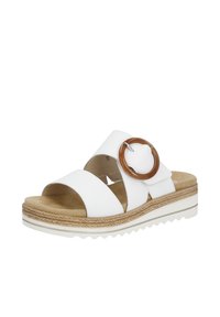 White slide sandals with two wide straps, a brown circular accent, textured footbed, and a layered sole for added height.