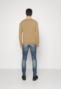 Světle hnědý pletený svetr s dlouhými rukávy, kombinovaný s úzkými modrými džíny. Jednoduchý design s kulatým výstřihem a žebrovanými manžetami. Černé boty.