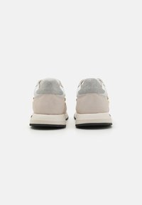Zapatillas grises y beige con una parte superior de ante texturizado y cuero suave, con acentos de hardware dorado y una suela de goma negra.