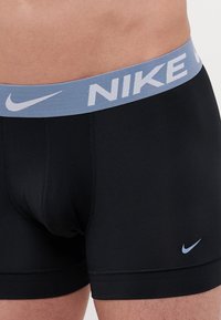 Crne Nike bokserice imaju svijetloplavi elastični pojas sa bijelim natpisom "NIKE" i malim plavim swoosh logotipom sprijeda.