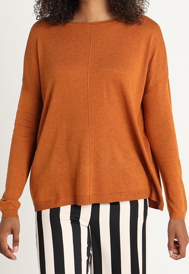 Femme portant un pull orange à manches longues et un pantalon à rayures verticales noires et blanches, coupé au niveau du cou et à mi-cuisse.