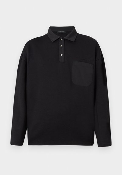 Svart langermet polo skjorte med knapper ved kragen, brystlomme og en subtil "Les Benjamins" logo på venstre brystområde.