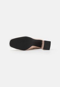 Nude højhælede sko med en tekstureret sort gummisål og et slankt design med en rund tå og en blokhæl for stabilitet.