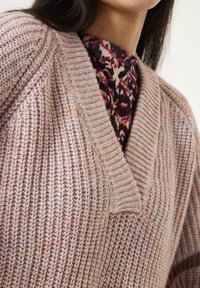 Leicht strukturiertes, gestricktes Sweatshirt in sanftem Rosaton, mit V-Ausschnitt und gerippten Akzenten. Übereinander getragen mit einem blumigen Oberteil.