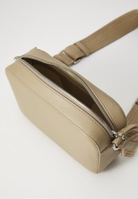 Borsa a spalla in pelle beige con forma rettangolare, chiusura con zip e tracolla strutturata. L'interno è spazioso e presenta una finitura liscia.