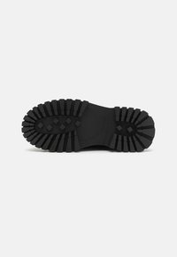 Suola di scarpa in gomma nera con motivi di battistrada profondi e multidirezionali e tasselli di trazione quadrati; design del tacco piatto e arrotondato.