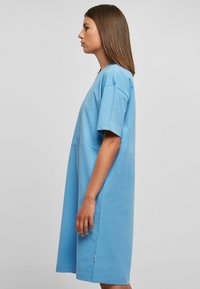 Svijetloplava oversized T-shirt haljina s kratkim rukavima, okruglim izrezom i glatkom pamučnom teksturom. Pada iznad koljena s detaljima na bočnim šavovima.