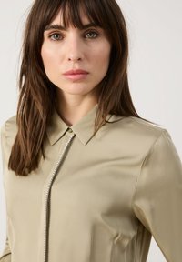 Khakifarbene Bluse mit Knöpfen und klassischem Kragen, ausgestattet mit einem Reißverschluss mit dekorativen Perlen, glattem Stoff und taillierter Passform.