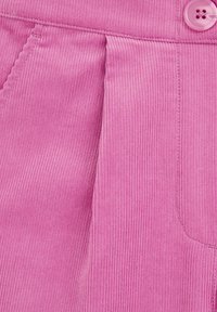 Närbild av rosa kordflorsduk med vertikala åsar, med en knappknäppning och veckdetalj på sidan.