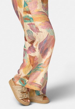 Vista a nivel de las piernas de un pantalón con un estampado abstracto de hojas en tonos pastel, combinado con sandalias beige de plataforma tejidas con hebillas de brillantes.