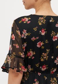 Robe noire à fleurs avec des manches courtes en tulle volantes, ornée d'un mélange de fleurs roses, jaunes et blanches sur un fond sombre.