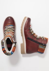 Botas de cuero rojo con un colorido cuello de punto decorado, cordones en la parte delantera y cremallera lateral con una suela de goma beige.