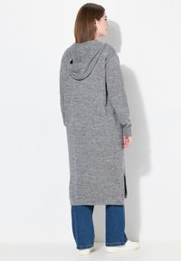 Lång grå stickad cardigan med huva, sidsprund och ribbade manschetter, ihop med blå vida jeans och vita sneakers.