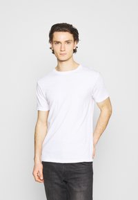 Camiseta blanca de manga corta hecha de algodón. Diseño clásico de cuello redondo, textura suave, con un aspecto liso y sin adornos.