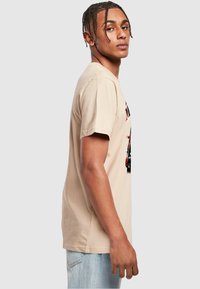 Tricou din bumbac bej cu un imprimeu grafic pe față. Mâneci scurte, gât rotund și o croială lejeră cu o textură netedă.