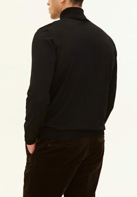 Maglione nero a collo alto in maglia con maniche lunghe e collo a coste, abbinato a pantaloni in velluto a coste marrone scuro. Tessuto liscio, design aderente.