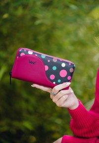 Magenta wallet with a black side featuring multicolored dots. Zipper closure with a curved accent on one side. Textured material.