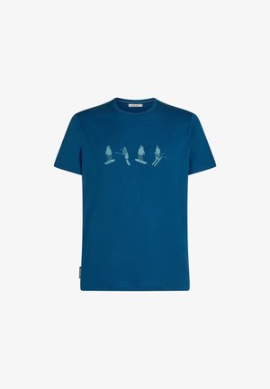 T-shirt bleu à manches courtes avec un graphique bleu clair représentant quatre figures de sports d'hiver : deux sur des planches à neige et deux en ski, dans différentes poses.