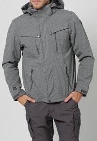 Graue, strukturierte Jacke mit Reißverschluss und Knopfverschluss, verstellbare Kapuze und mehreren Fronttaschen. Der Stoff scheint wetterbeständig zu sein.