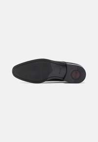 Talpa unei pantofi de dress din piele neagră, cu suprafață texturată pentru aderență și logo-ul "ALDO" pe tocul pantofului, pe un fundal alb simplu.