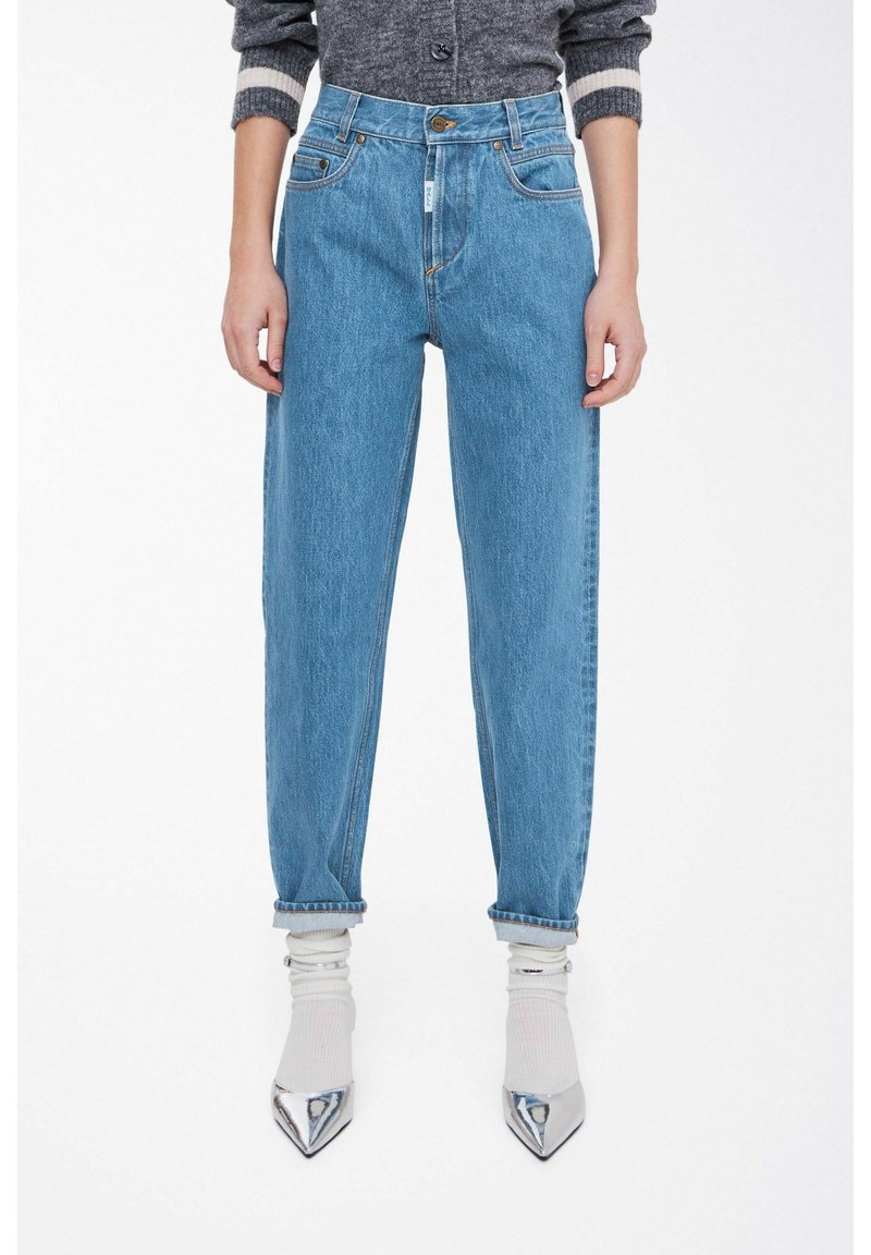 Jeans in denim azzurro chiaro a vita alta con gambe affusolate, design a cinque tasche e orli arrotolati, abbinati a un maglione grigio e scarpe appuntite.