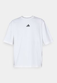 T-shirt en coton blanc avec un logo Adidas noir sur la poitrine, à manches courtes, un col rond et des fentes sur les côtés à l'ourlet.