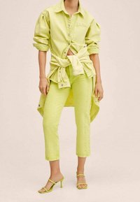Camisa de mezclilla verde lima superpuesta sobre pantalones cortos a juego, con un ajuste holgado, cierre de botones y mangas enrolladas. Combinada con sandalias ajustadas.