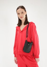 Rød hættebluse med frontlomme og ribbet krave, parret med en sort tekstureret crossbody-taske med en gylden trykknap.