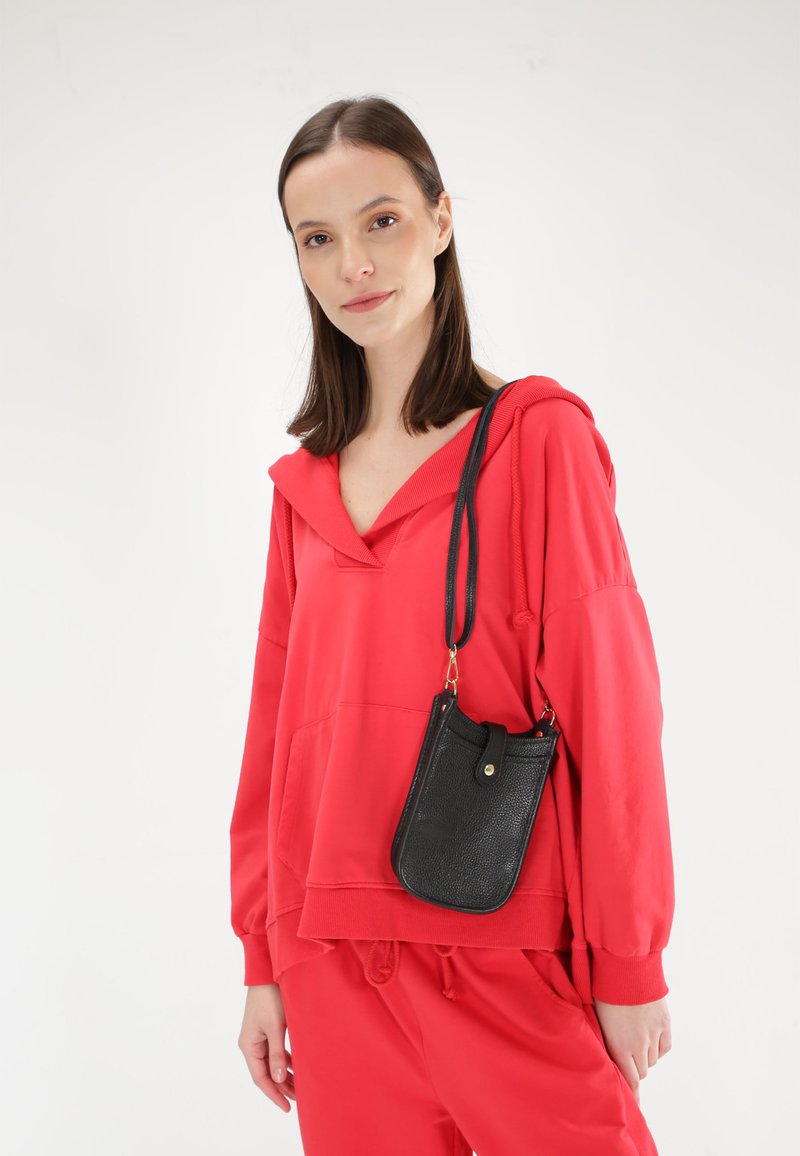 Rød hættebluse med frontlomme og ribbet krave, parret med en sort tekstureret crossbody-taske med en gylden trykknap.