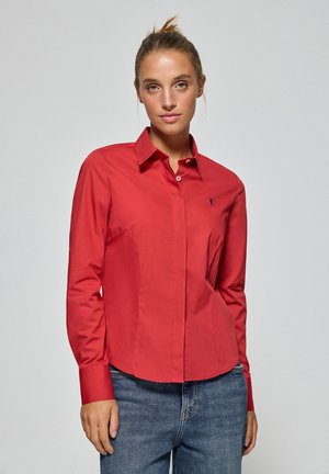 Chemise rouge à boutons avec un col structuré, des manches longues et un ourlet incurvé. Présente un petit logo contrasté sur la poitrine.
