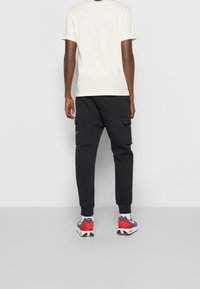 Vaaleanbeige t-paita, mustat cargo-housut taskuilla ja punaiset, siniset ja valkoiset lenkkarit. Yksinkertainen, rento muotoilu ja mukava istuvuus.