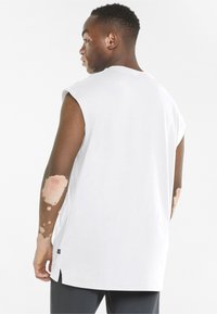 Hvid ærmeløs t-shirt med rund halsudskæring, sideslids og et lille sort mærke ved kanten. Glat bomuldsstof.
