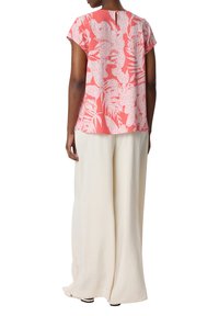Blusa rosa a maniche corte con motivi bianchi, dettaglio a chiave sul retro, abbinata a pantaloni larghi crema realizzati in un tessuto testurizzato.