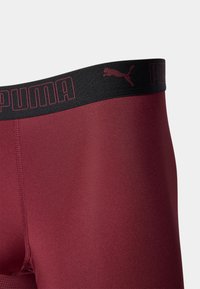 Bordó sportnadrág fekete elasztikus derékkal, amelyen a „PUMA” logó és logó sziluett van domborítva. Simább textúra és testhezálló kialakítás.