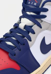 La sneaker presenta una combinazione di pelle rossa, blu e bianca con lacci blu testurizzati, una linguetta imbottita e il logo Nike swoosh nero.