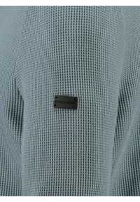 Maglione a lavagna blu chiaro, in lavorazione a maglia testurizzata con motivo a nido d'ape. Presenta un piccolo etichetta nera cucita di lato, con la scritta "KEY LARGO".