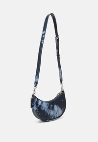 Torba na ramię z tkaniny tie-dye w odcieniach ciemnoniebieskiego i jasnoniebieskiego, o zakrzywionym kształcie, z regulowanym paskiem i srebrnymi akcentami metalowymi.