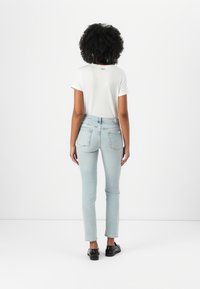Witte korte mouwen t-shirt, lichtblauwe slim-fit jeans en zwarte schoenen. Eenvoudig ontwerp met logo detail op de rug en standaard zakindeling.