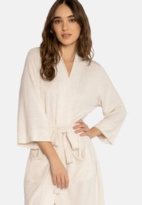 Robe color crema realizzato in tessuto morbido, dotato di una cintura da annodare, due tasche frontali e maniche larghe. Texture liscia con un leggero motivo.