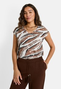 Top de manga corta en una mezcla de estampado animal en blanco y marrón, con escote en V y un corte relajado, combinado con pantalones de cintura elástica marrones.