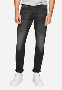Pantalones vaqueros de denim negro con corte slim, detalles de desgaste, diseño de cinco bolsillos y puños enrollados, combinados con zapatillas blancas.