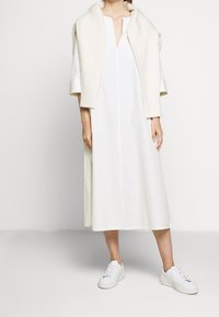 Bílá šaty po kolena se přímým střihem a krátkými rukávy, doplněné krémovým pleteným šálkem. Nosí se s bílými teniskami.