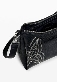 Borsa in pelle nera текстurizzata con hardware argentato, con motivo floreale ricamato e apertura con zip. Include una tracolla rimovibile.