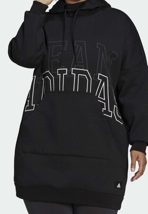 Osoba nosząca czarną, dużą bluzę z kapturem Adidas z dużą przednią kieszenią i wyraźnym napisem "ADIDAS" na piersi.