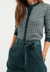 Knapp-up tröja med ett vågmönster i grönt och vitt, med rund halsringning och ribbade manschetter, i kombination med teal högmidjade byxor.