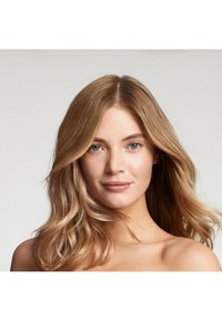 Naturligt hår med vågig textur, i nyanser av ljusbrunt och blont. Klara blå ögon och en mjuk hy. Neutral bakgrund.