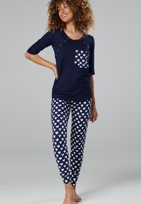Navy cotton pajama set featuring a short-sleeve top with a buttoned pocket and white heart patterns on fitted pants. Soft, relaxed fit.