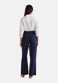 Chemise en lin à manches retroussées et empiècement dans le dos, associée à un pantalon large bleu marine doté d'une taille élastique et de deux poches arrière.