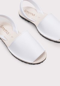 Sandalias abiertas blancas con parte superior sintética suave, suela de goma negra y correas ajustables para un ajuste seguro. Diseño minimalista con detalles de costura.