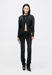 Μαύρο τζάκετ από τζιν με στυλ cropped, που διαθέτει κουμπιά περιτύλιξης και τσέπες στο στήθος, συνδυασμένο με μαύρα τζιν slim-fit και μυτερά τακούνια.